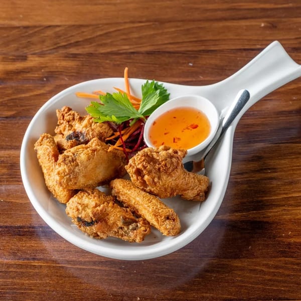 Crispy fried chicken wings with a side of sweet chili dipping sauce and garnish on a white plate.