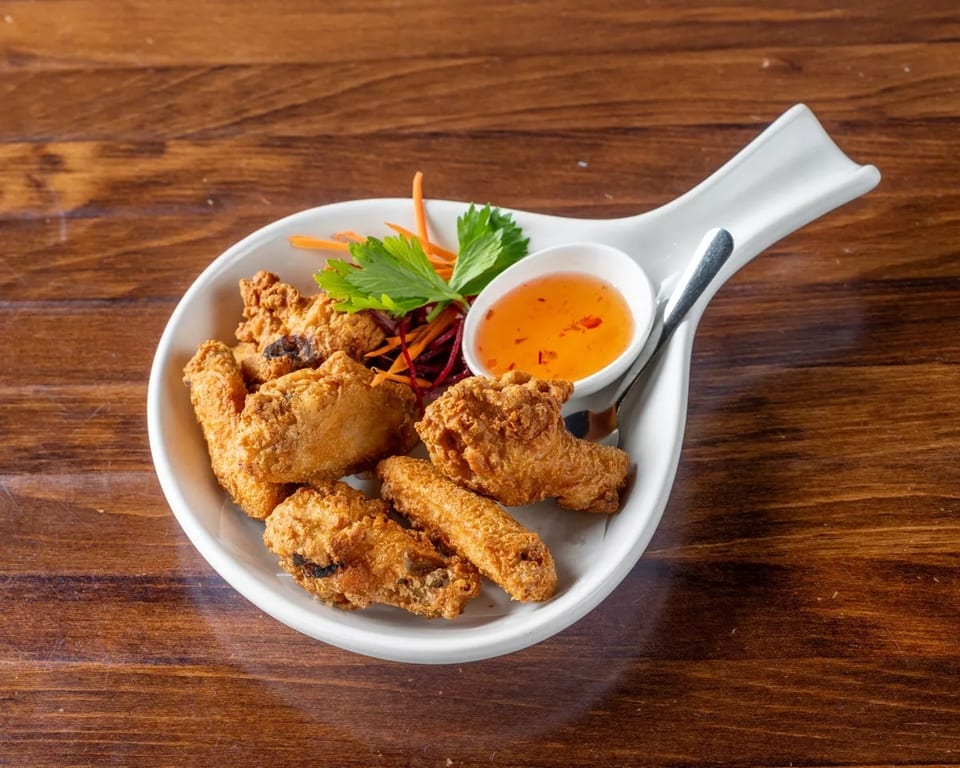 Crispy fried chicken wings with a side of sweet chili dipping sauce and garnish on a white plate.