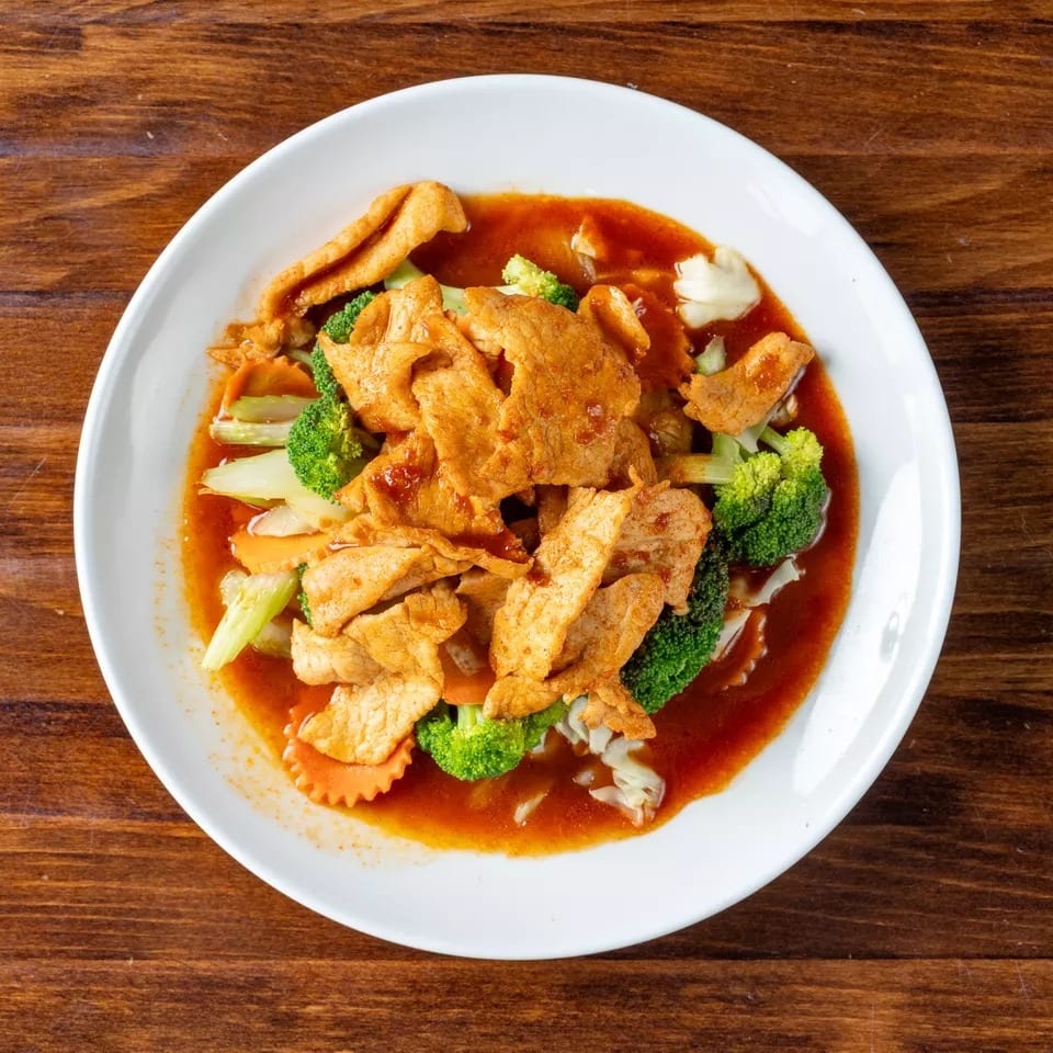 Spicy chicken and mixed vegetables in a red sauce, served on a white plate.