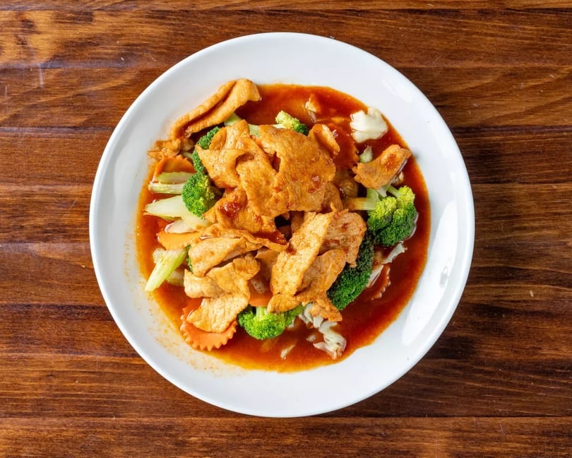 Spicy chicken and mixed vegetables in a red sauce, served on a white plate.