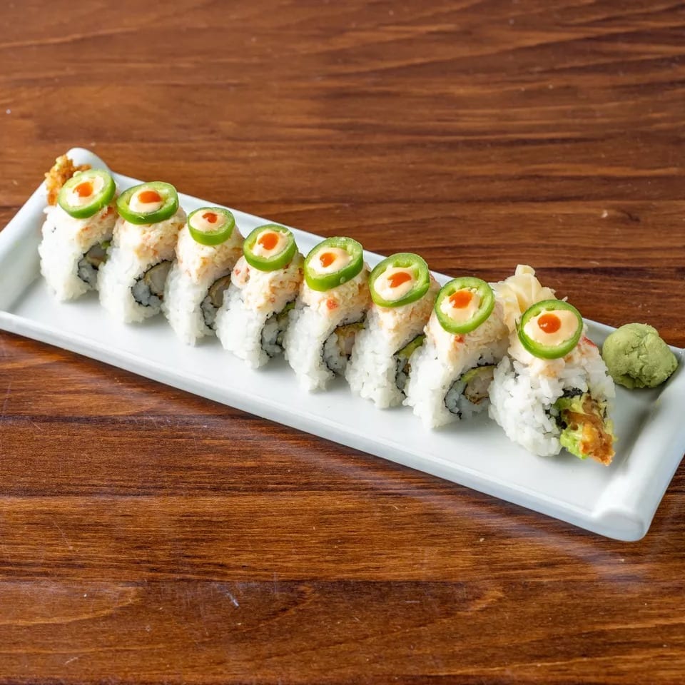 Sushi roll with crab, avocado, and jalapeño slices on a white plate with wasabi and ginger.