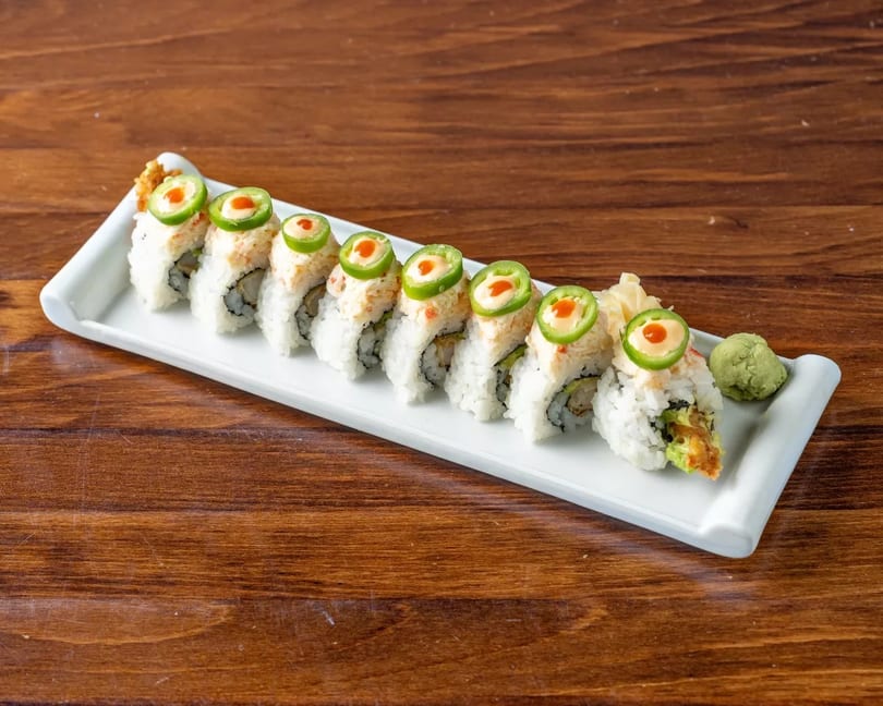 Sushi roll with crab, avocado, and jalapeño slices on a white plate with wasabi and ginger.