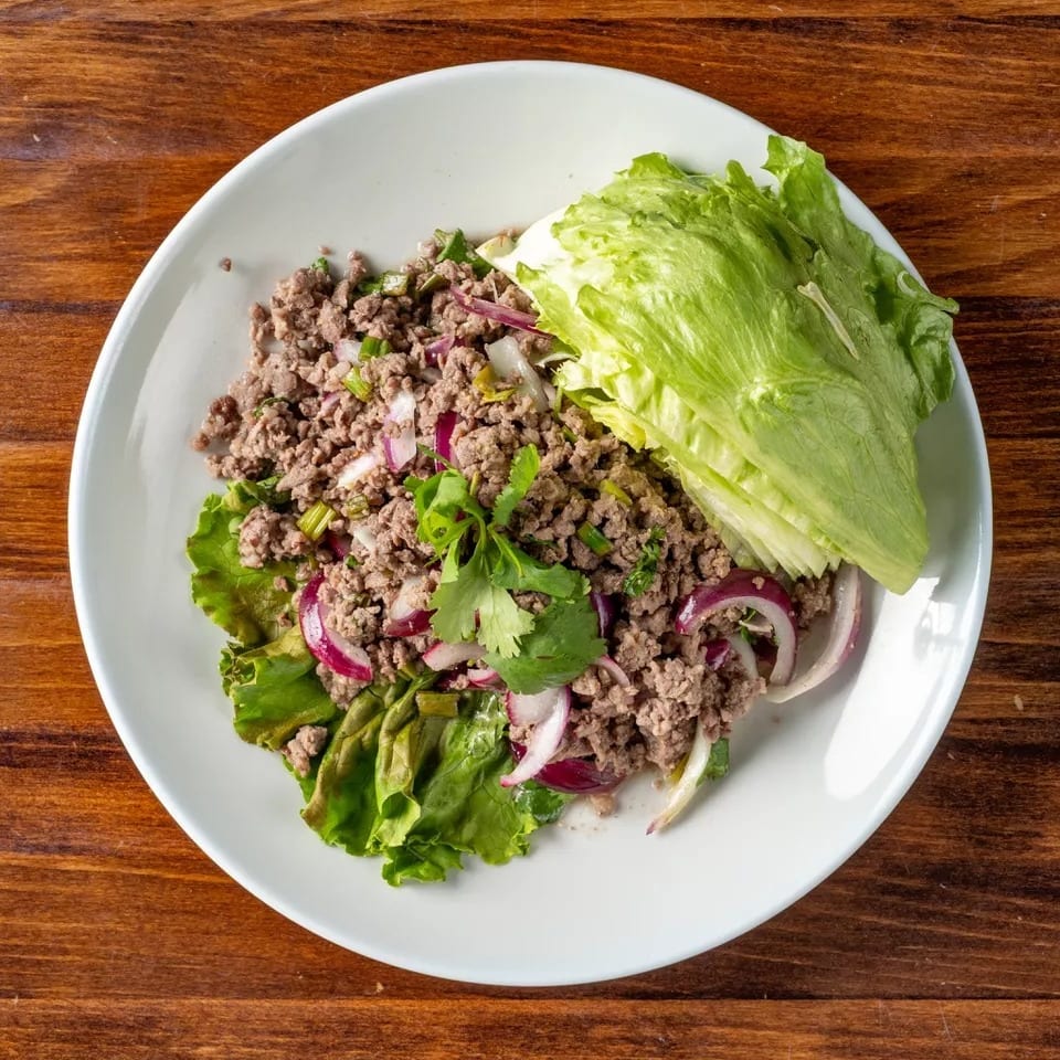 Larb, a Thai minced meat salad with red onions, cilantro, and lettuce wraps on a white plate.