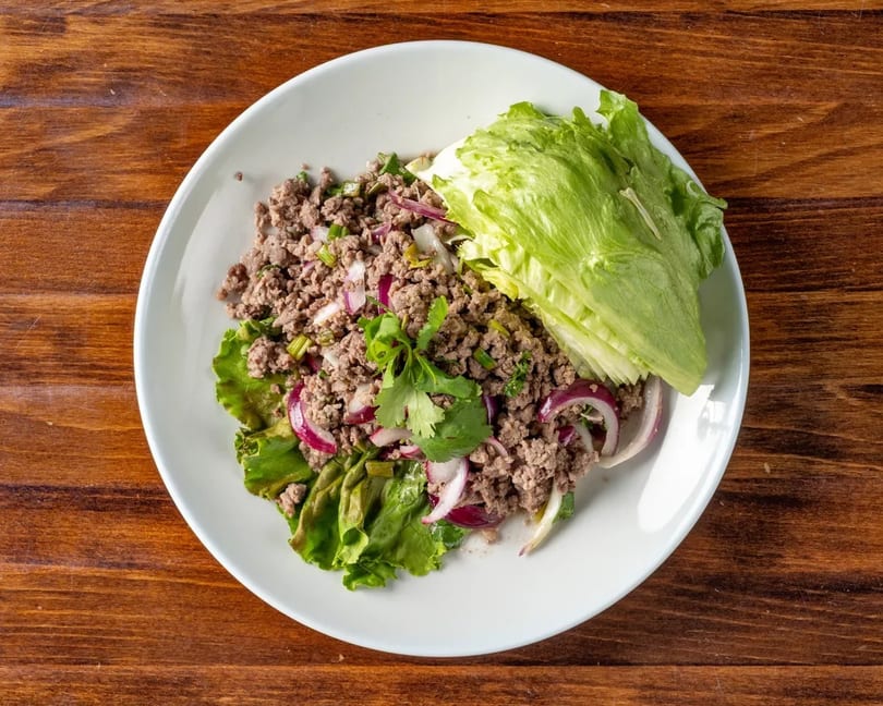 Larb, a Thai minced meat salad with red onions, cilantro, and lettuce wraps on a white plate.