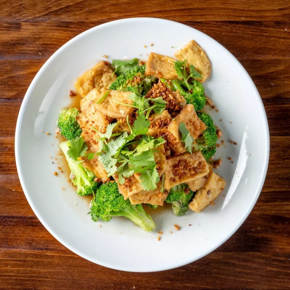 Crispy tofu and vibrant green broccoli florets topped with fresh cilantro and garlic on a white plate.