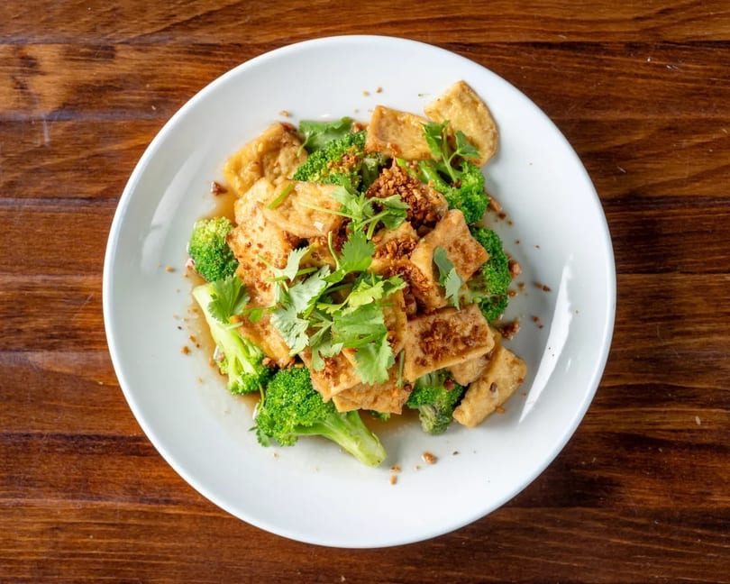 Crispy tofu and vibrant green broccoli florets topped with fresh cilantro and garlic on a white plate.