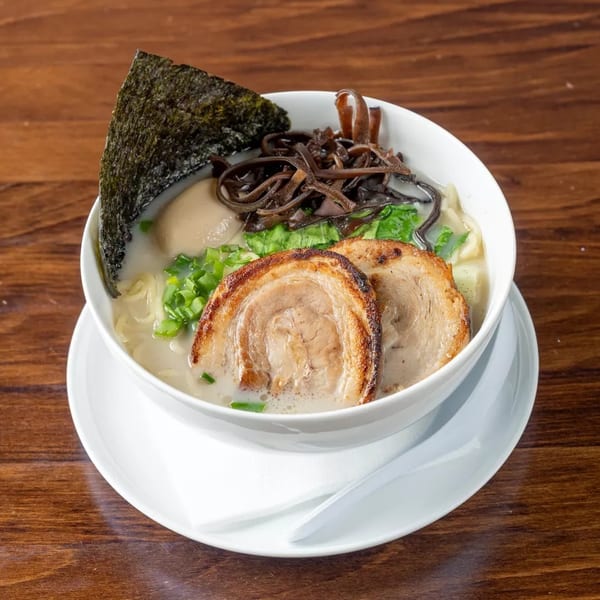 A bowl of ramen with pork, egg, seaweed, and mushrooms on a wooden table.