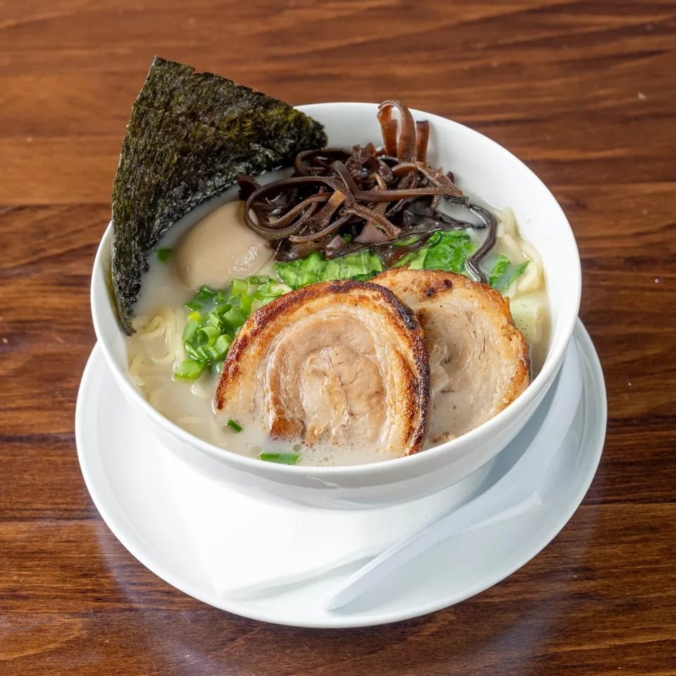 A bowl of ramen with pork, egg, seaweed, and mushrooms on a wooden table.