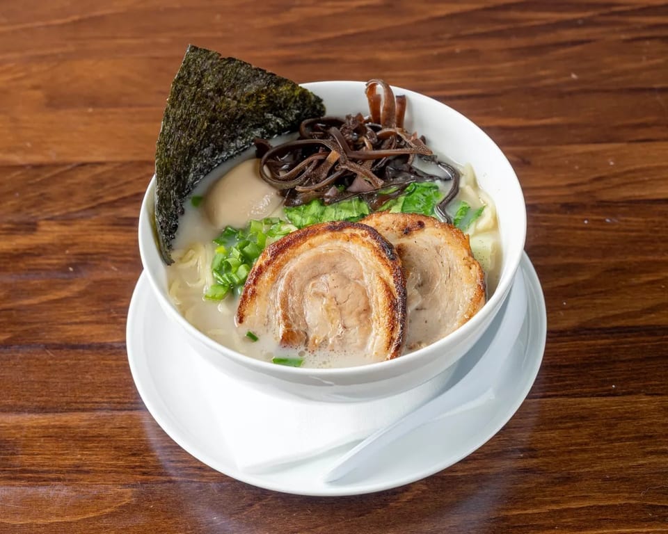 A bowl of ramen with pork, egg, seaweed, and mushrooms on a wooden table.