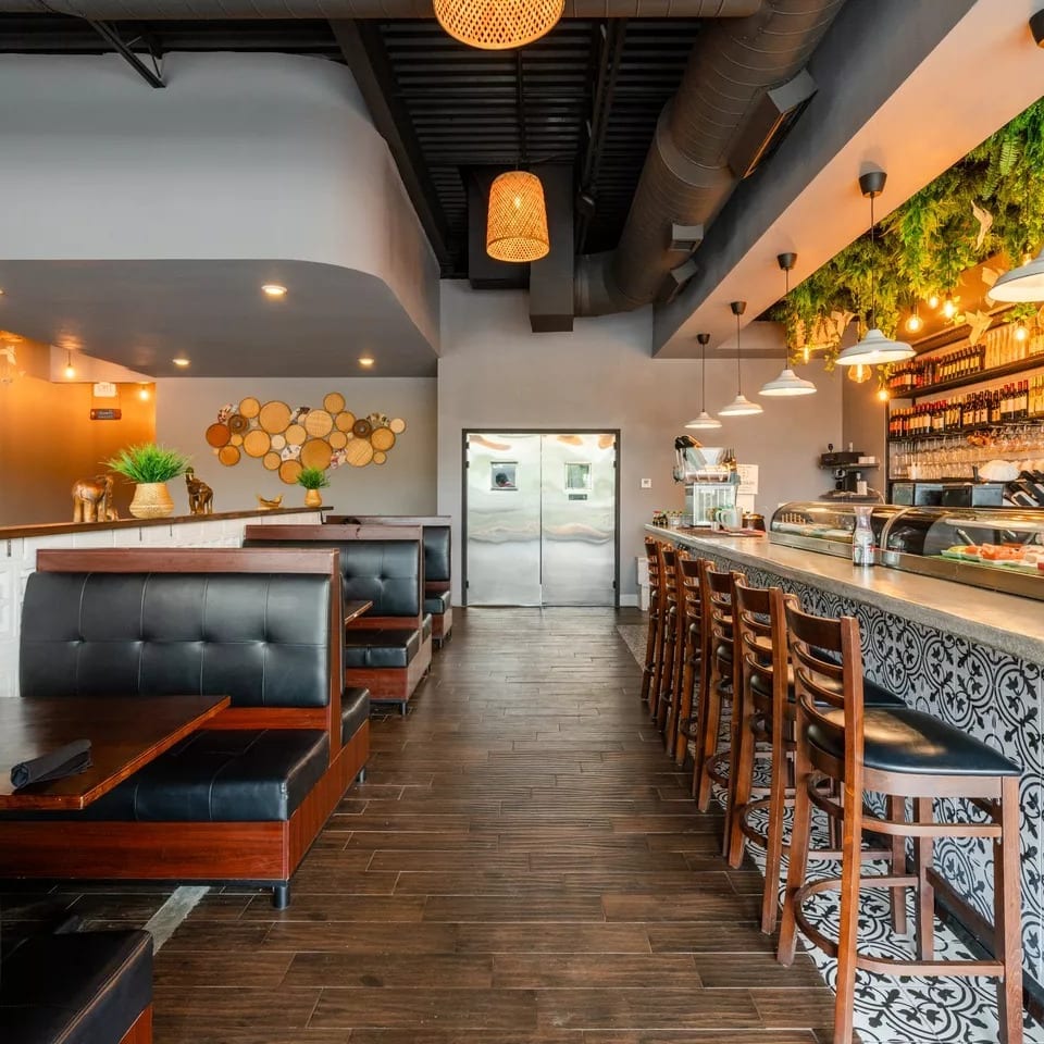 Modern restaurant interior with booth seating, a long bar with stools, and decorative lighting.