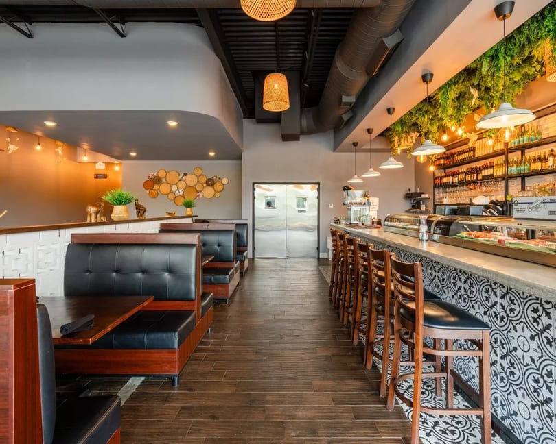 Modern restaurant interior with booth seating, a long bar with stools, and decorative lighting.
