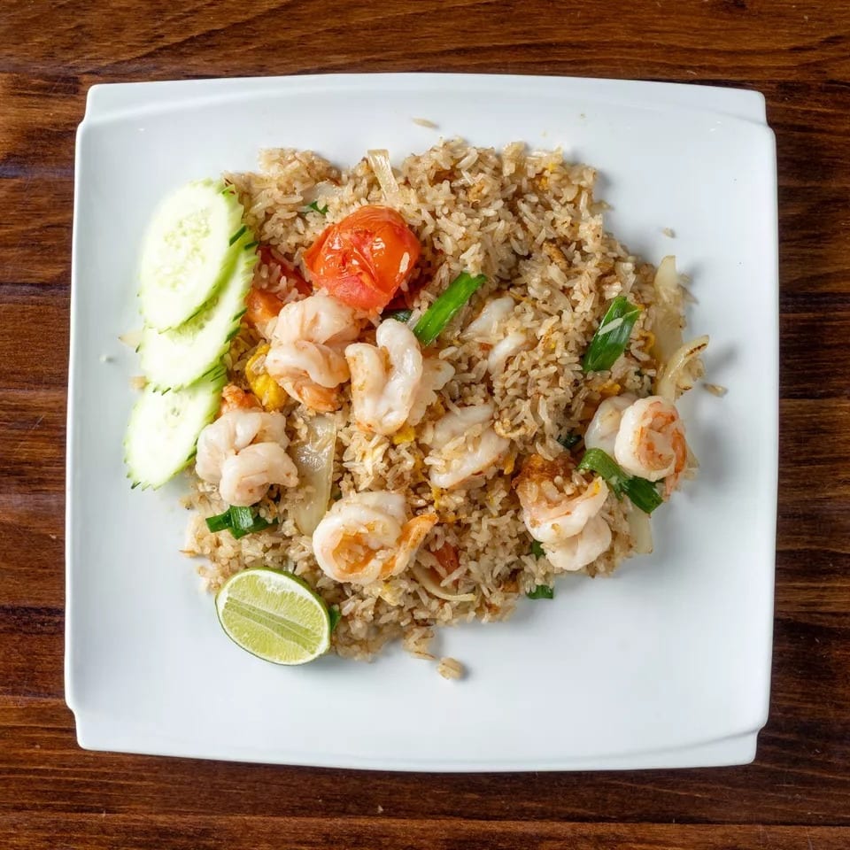 Shrimp fried rice with cucumber slices, a lime wedge, and roasted tomato on a white plate.