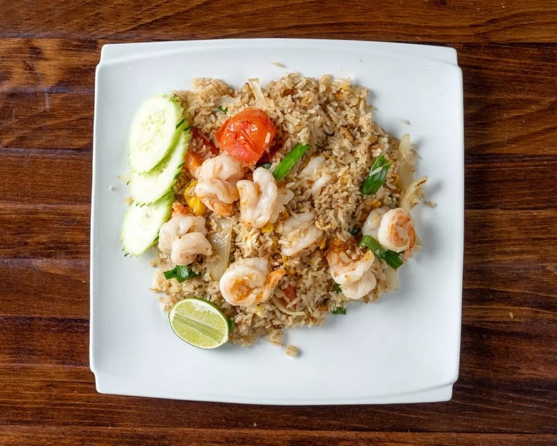Shrimp fried rice with cucumber slices, a lime wedge, and roasted tomato on a white plate.