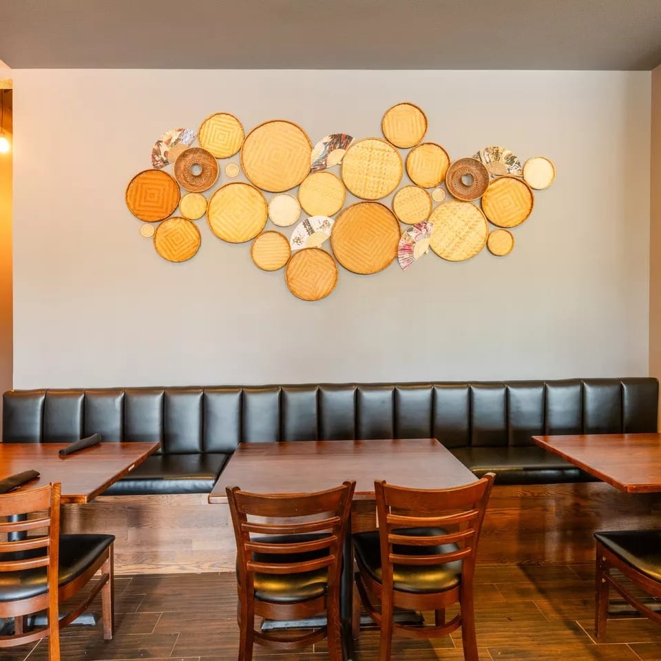 Restaurant dining area with dark leather booth seating, wooden tables, and decorative woven plates on the wall.