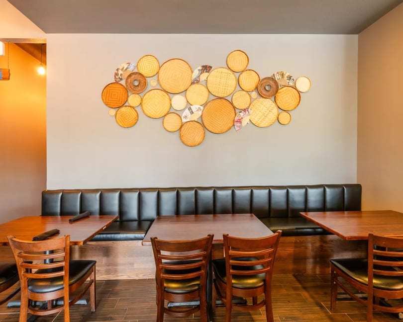 Restaurant dining area with dark leather booth seating, wooden tables, and decorative woven plates on the wall.
