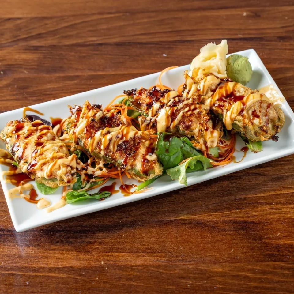 Fried jalapeño poppers drizzled with sauce, served on a bed of greens with ginger and wasabi.