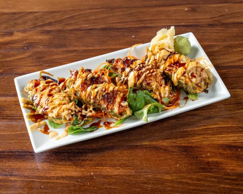 Fried jalapeño poppers drizzled with sauce, served on a bed of greens with ginger and wasabi.