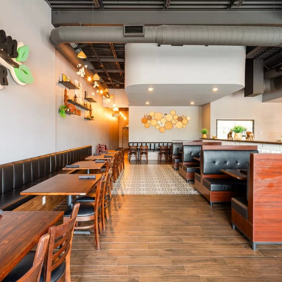 Spacious, modern restaurant interior with long banquette seating, wooden tables, and booth seating, featuring a bar area.