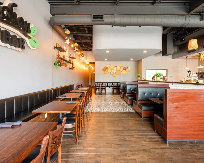 Spacious, modern restaurant interior with long banquette seating, wooden tables, and booth seating, featuring a bar area.