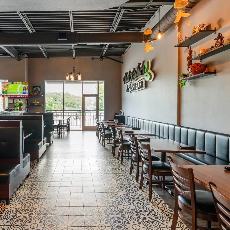 Modern restaurant interior with patterned floor, booth seating, wooden tables, and decorative wall shelves.