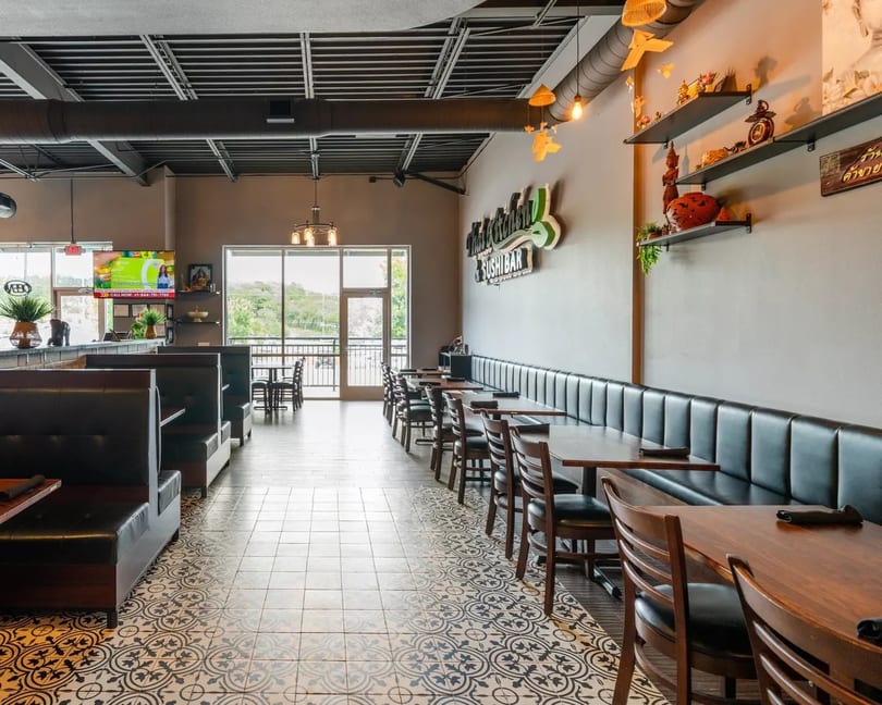 Modern restaurant interior with patterned floor, booth seating, wooden tables, and decorative wall shelves.